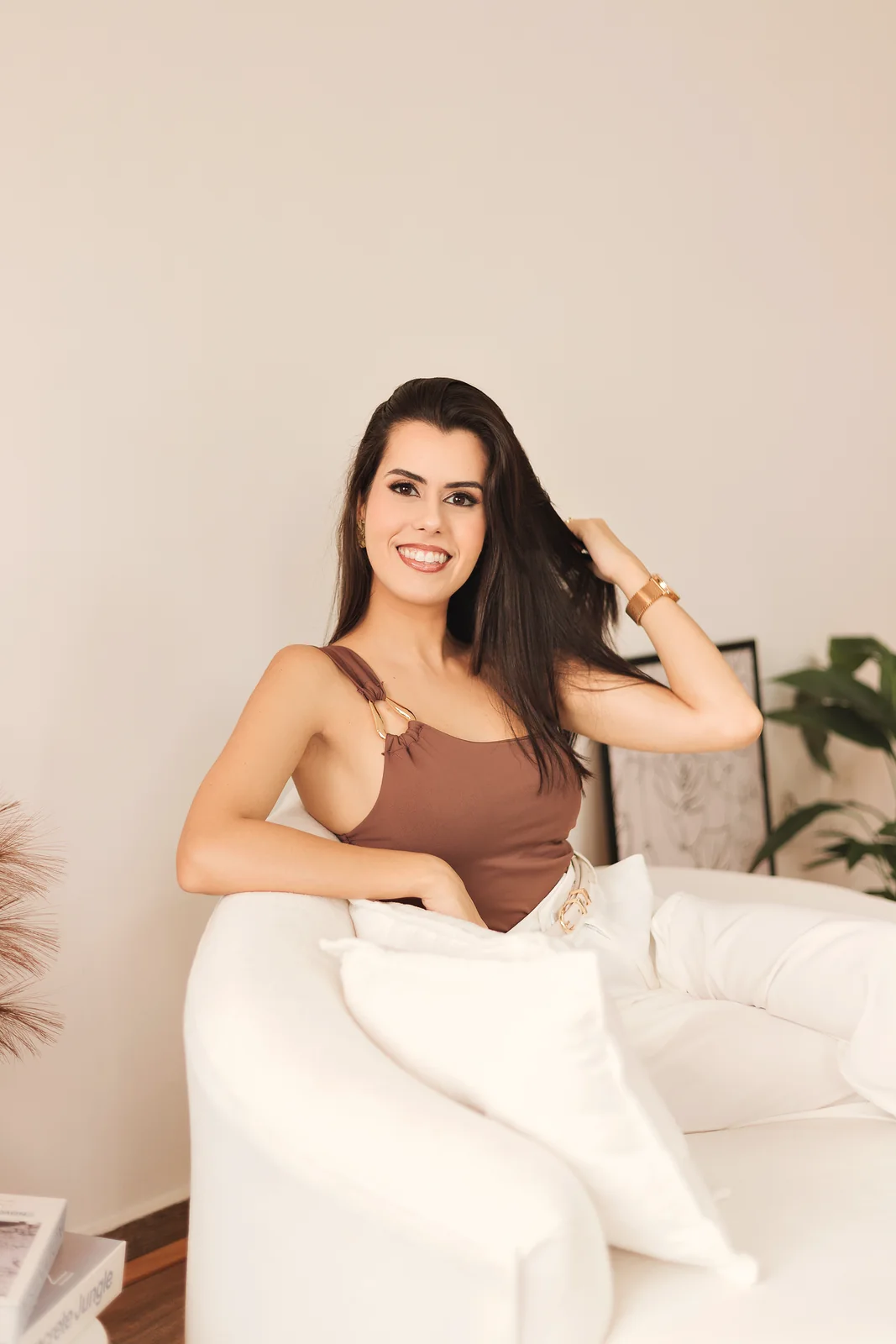 Dra. Flávia sentada no sofá, sorrindo, com a mão no cabelo