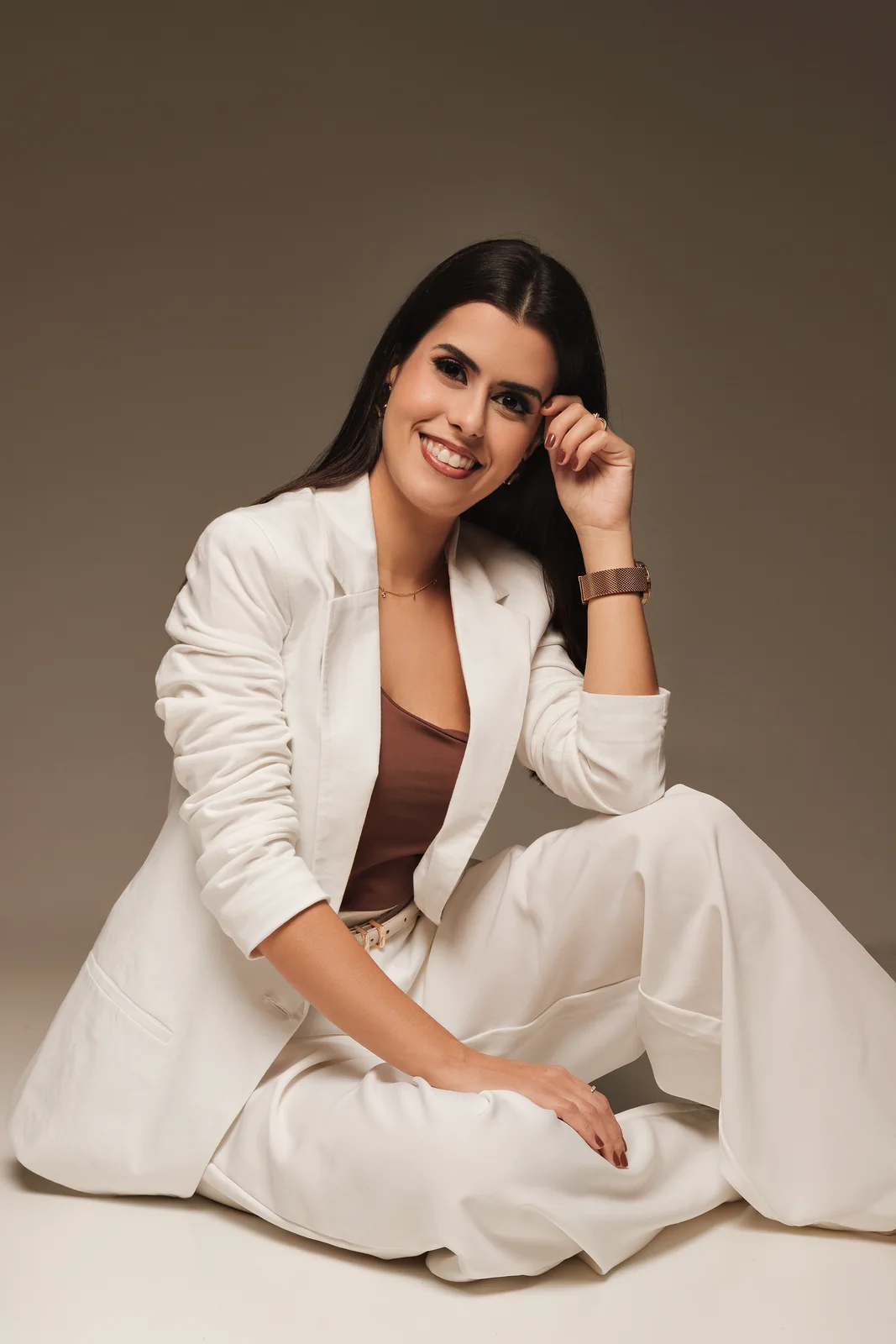 Dra. Flávia Mucci sentada, de terno branco, sorrindo para a câmera