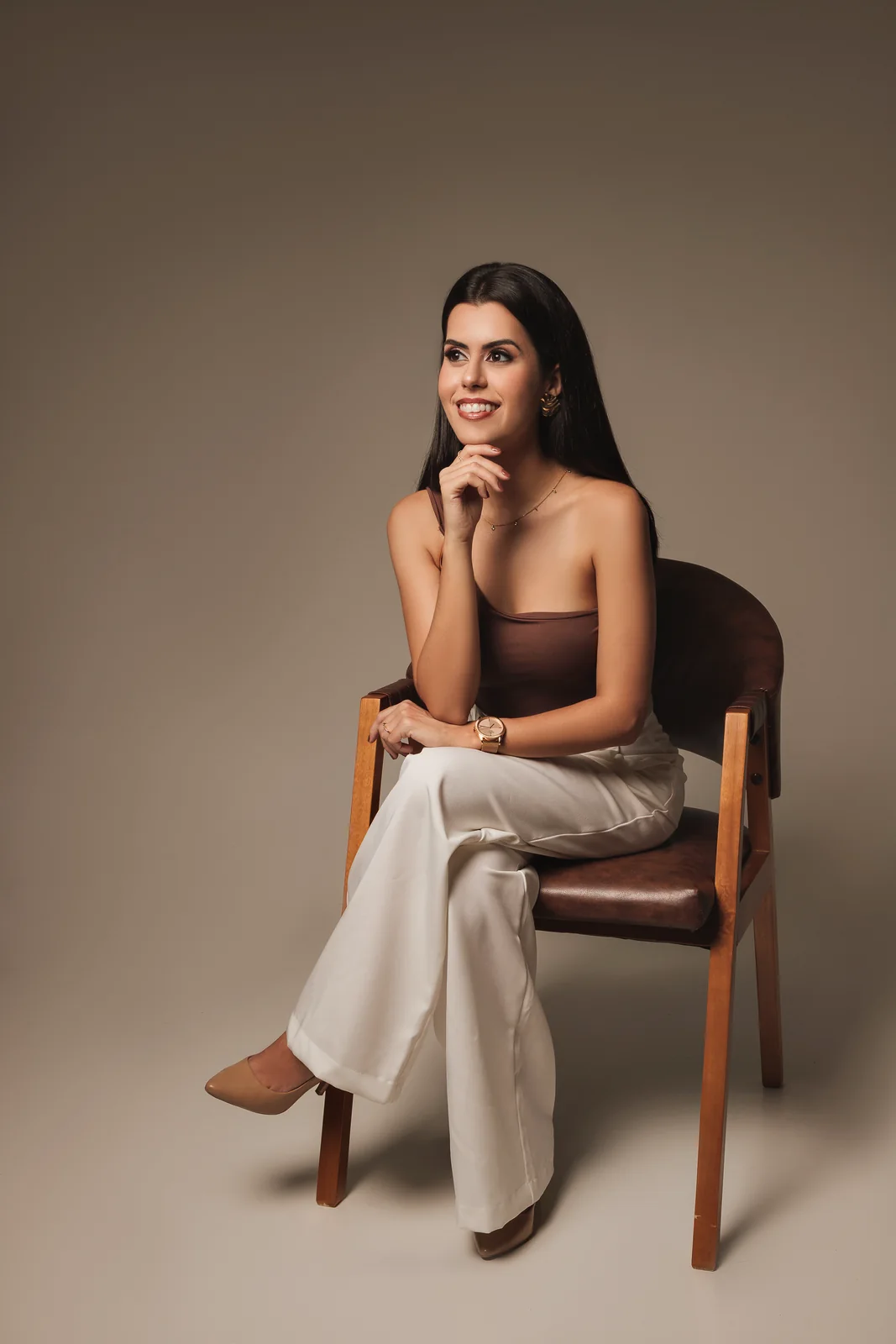 Dra. Ana Flávia Mucci sentada em uma cadeira de madeira, de calça branca